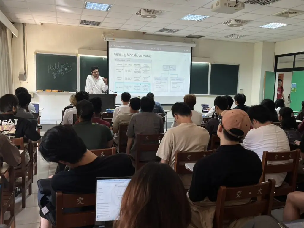Speaker presenting a slide on Sensing Modalities Matrix to a full classroom of students during a lecture.