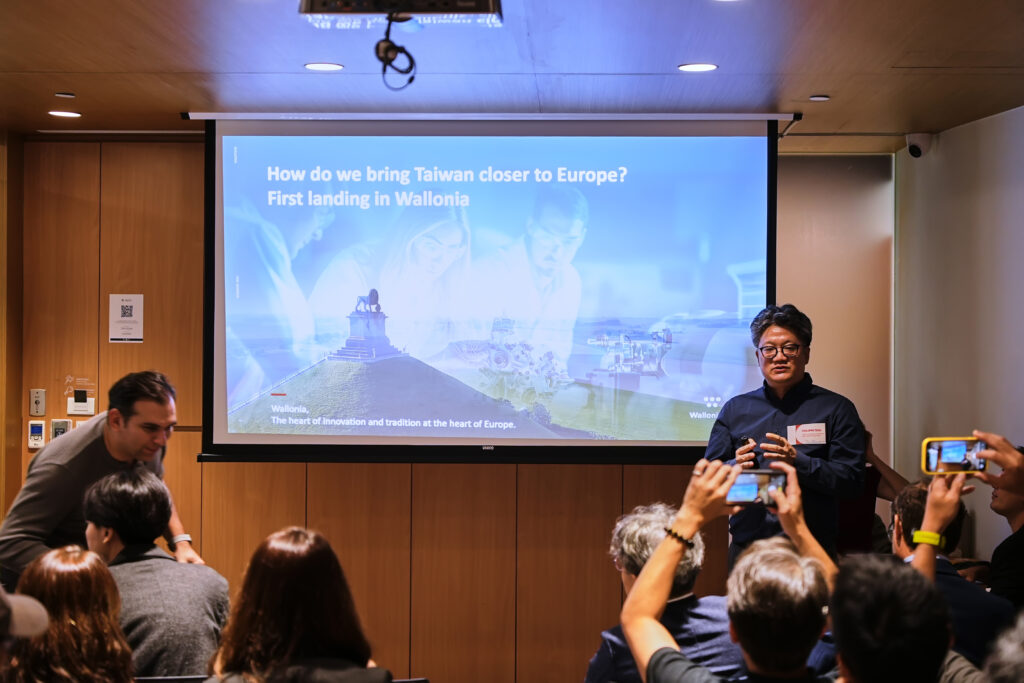 Presenter speaks near a screen showing a presentation about bringing Taiwan closer to Europe and Wallonia.
