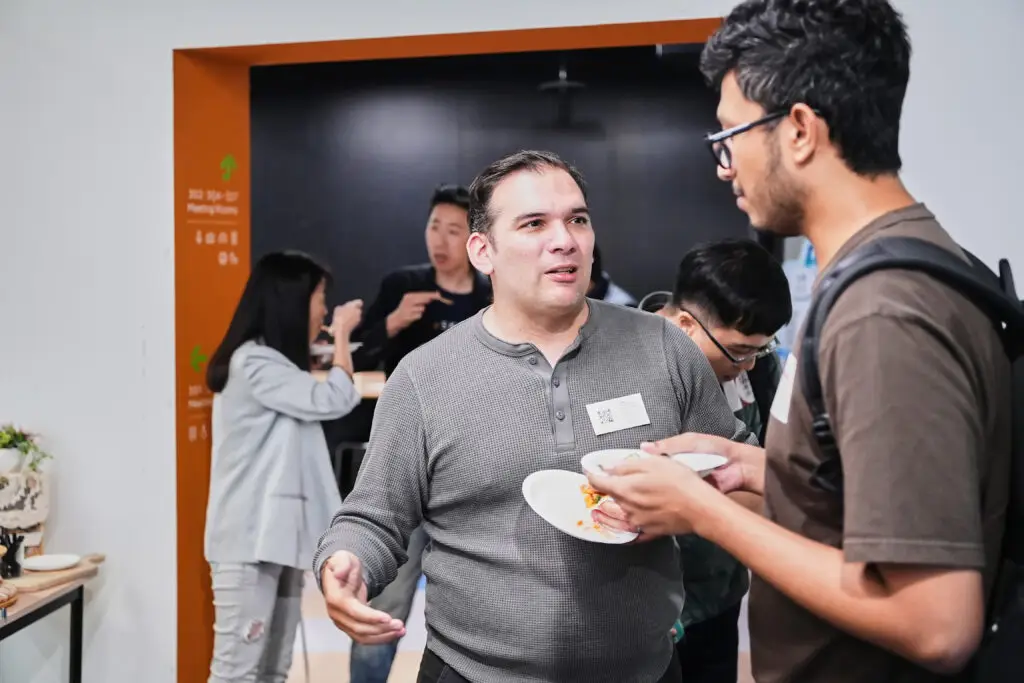 Two professionals conversing and holding plates of food at a business networking event.